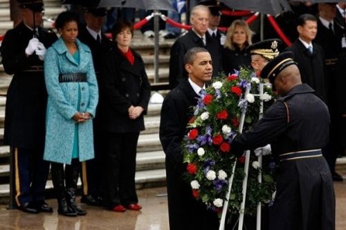 Michelle Obama, ever fashion forward in her signature ammo belt and wearing the cheerful colors that always characterize her wardrobe when she is celebrating the deaths of, um, attending the memorial services of U.S. soldiers who have died in the service of their country, stands next to Jill Biden and watches her husband performing the traditional ceremony of laying a wreath on Veteran's Day at Arlington National Cemetery.