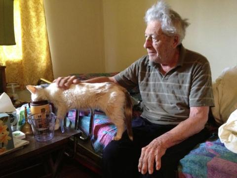 Hubert P. Yockey lets an elderly calico cat named Cleo drink from a mug of water at his bedside.