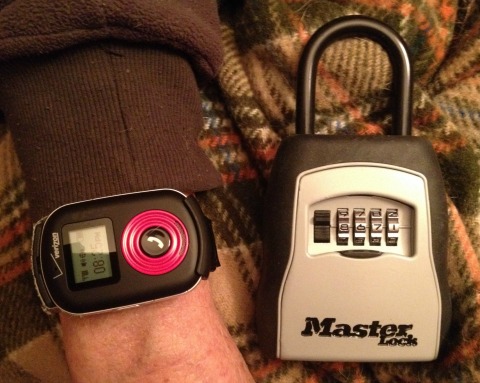 The Verizon SureResponse device in its wrist strap holder on my dad's wrist, next to a combination lockbox. The combination is usually shielded by a shutter that goes up to hide it.
